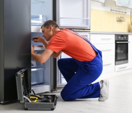 Male Technician With Screwdriver Repairing Refrigerator In Kitch